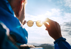 Backpacker man looking at bright sun through polarized sunglasses enjoying mountain landscape. Eye & Vision Care human health concept image.