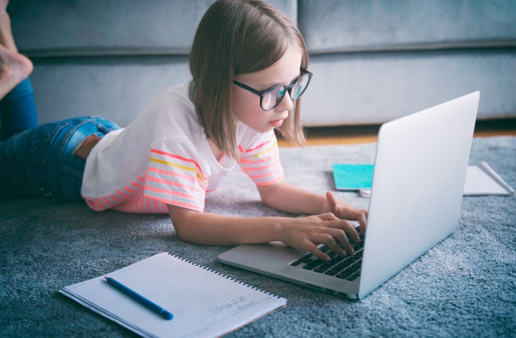 A child wears glasses and they do homework on a laptop