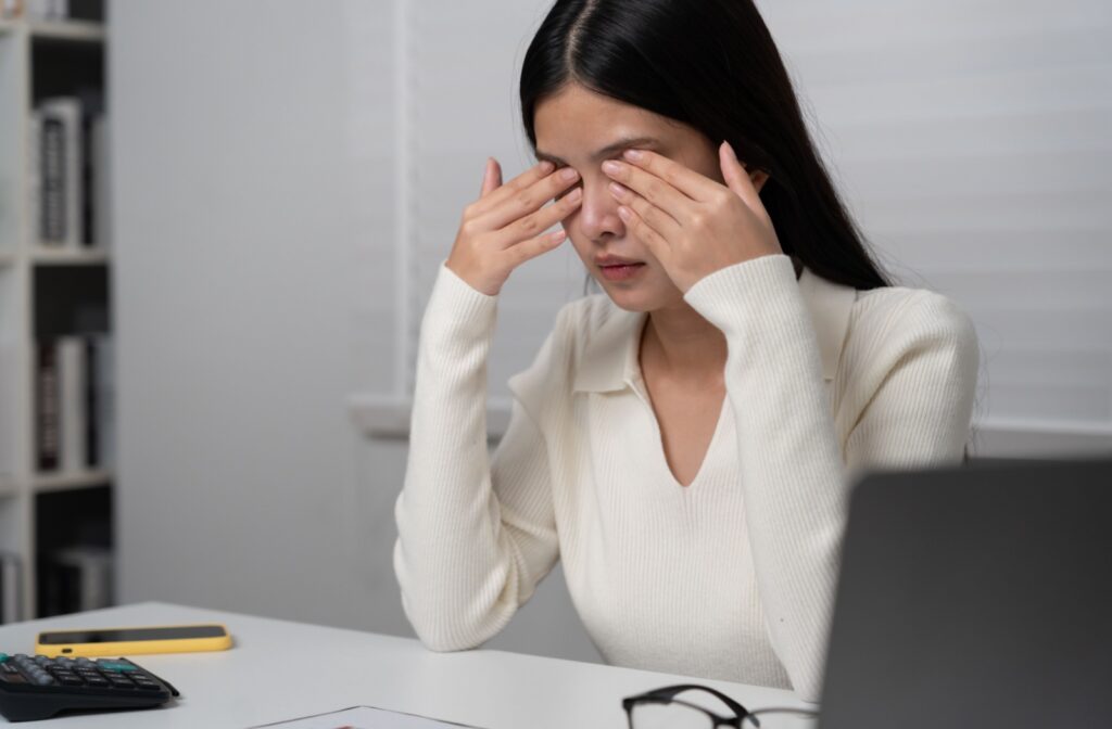 Person sitting in front of a computer at a desk rubbing their dry eyes