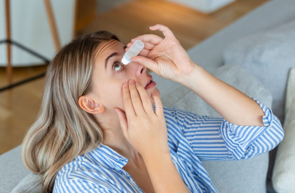 A person sitting on a couch looks up as they use eye drops on their dry eye