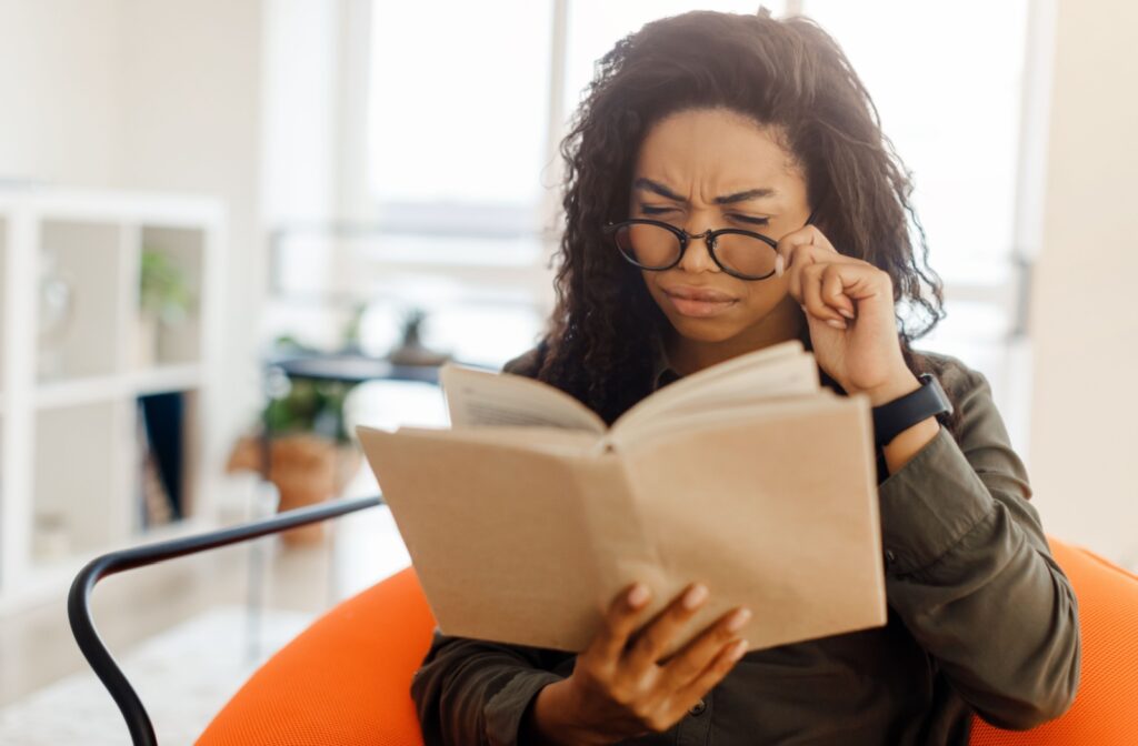 A person holding their glasses down their face while they read a book